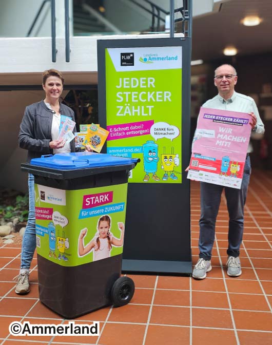 Eine Frau und ein älterer Mann, präsentieren eine Tonne, Plakat, Flyer und Werbetafel mit Werbebotschaften von PlanE mit Batti und Stecki.